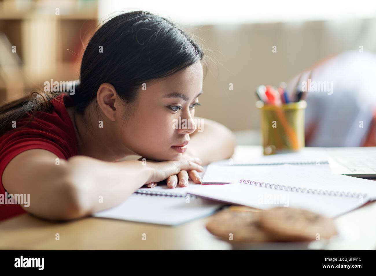 Noioso stanco triste teen studente cinese studentessa da solo, si trova a tavola con cookie, guarda notebook in camera Foto Stock