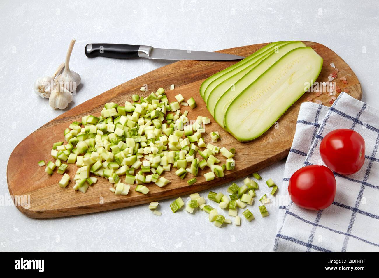 Zucchine a dadini tagliate a fette su un tagliere di legno, pomodori, aglio su un tavolo in cemento leggero Foto Stock