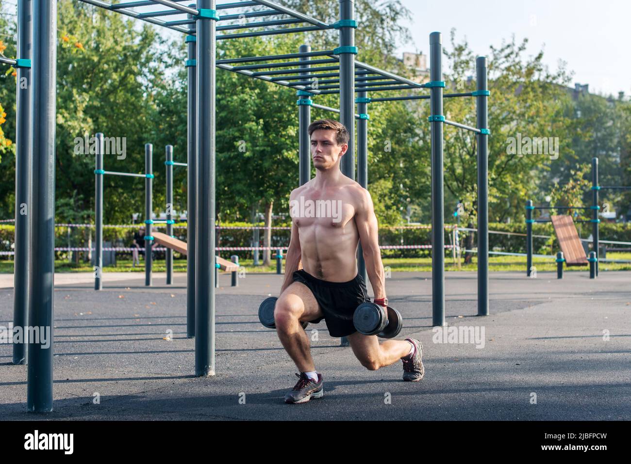 Giovane muscoloso fitness modello maschile facendo esercizi di affondo dumbbell nel parco Foto Stock