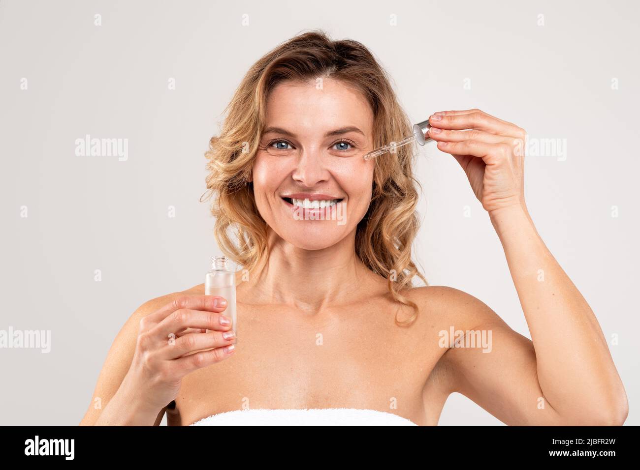 Cosmetici anti-età. Attraente Donna di mezza età applicando il siero della faccia sulla guancia Foto Stock