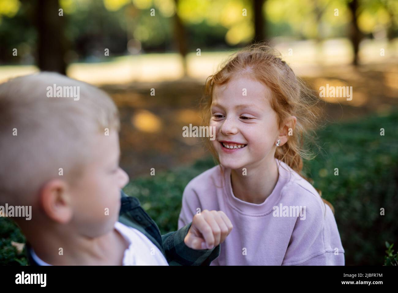 Ragazza piccola felice con le freckles e capelli rossi divertimento con suo fratello e sorridente all'aperto nel parco. Foto Stock