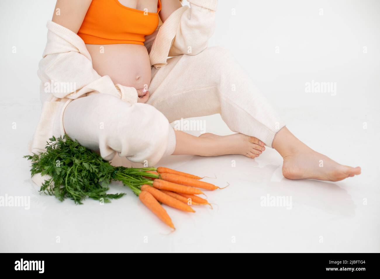Foto ritagliata di donna incinta seduta con fascio di verdure arancioni, carote verdi. Dieta alimentare fresca Foto Stock