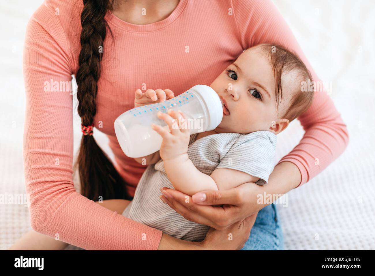 Ritratto di primo piano della madre con il bambino sulle mani, il bambino che tiene il biberon e bere il latte a casa Foto Stock