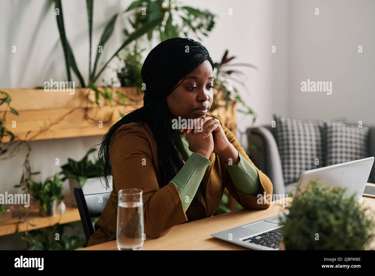 Giovane psicoanalista femminile che guarda la paziente durante una sessione online mentre si siede sul posto di lavoro di fronte al laptop in ufficio Foto Stock