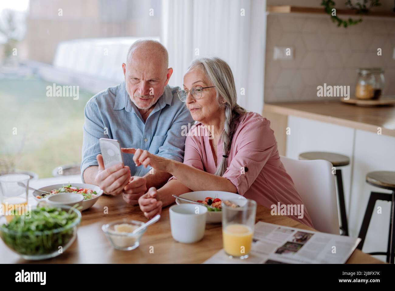 Una coppia anziana felice che usa lo smartphone durante la cena insieme a casa. Foto Stock