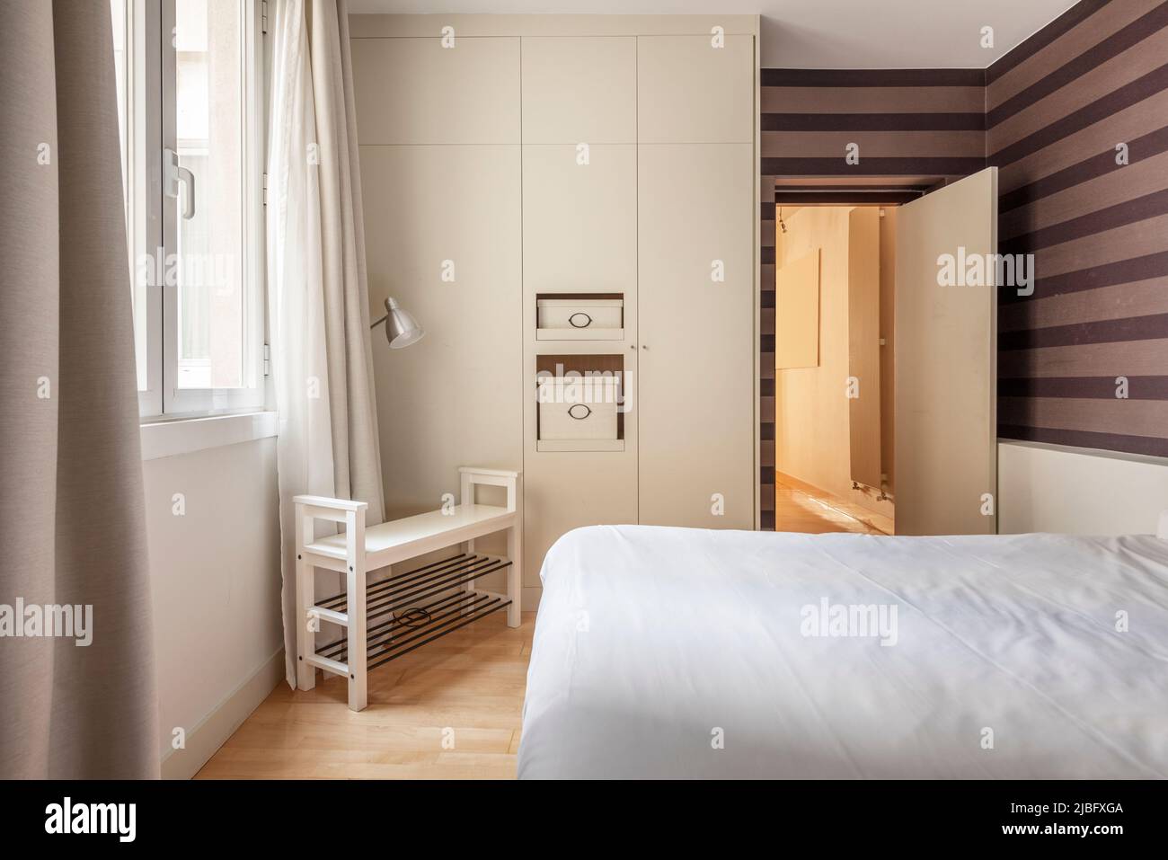 camera matrimoniale con armadi a muro, pareti con carta da parati decorativa a righe e armadio in legno per scarpe Foto Stock