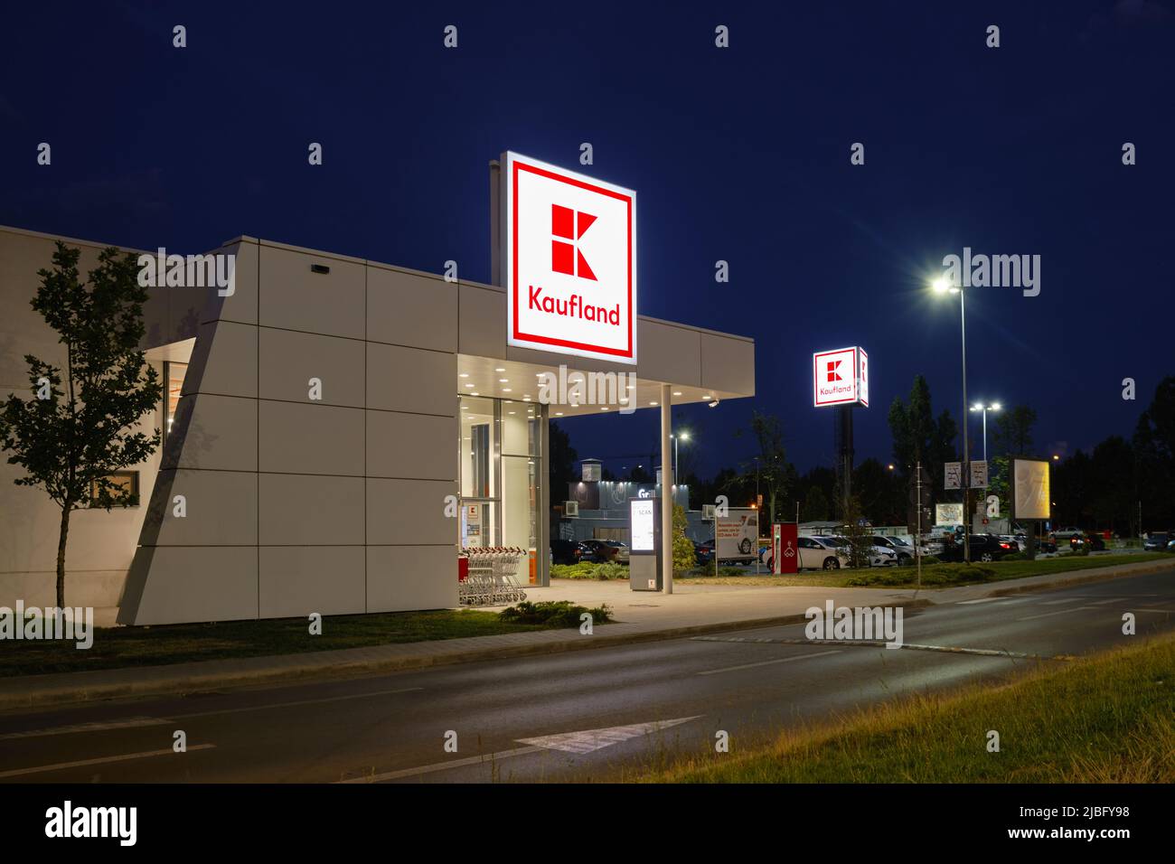 Cartello con il logo Kaufland e moderno edificio di negozi, di notte, con auto di passaggio. Kaufland è una catena di ipermercati tedesca, facente parte del gruppo Schwarz. Buch Foto Stock