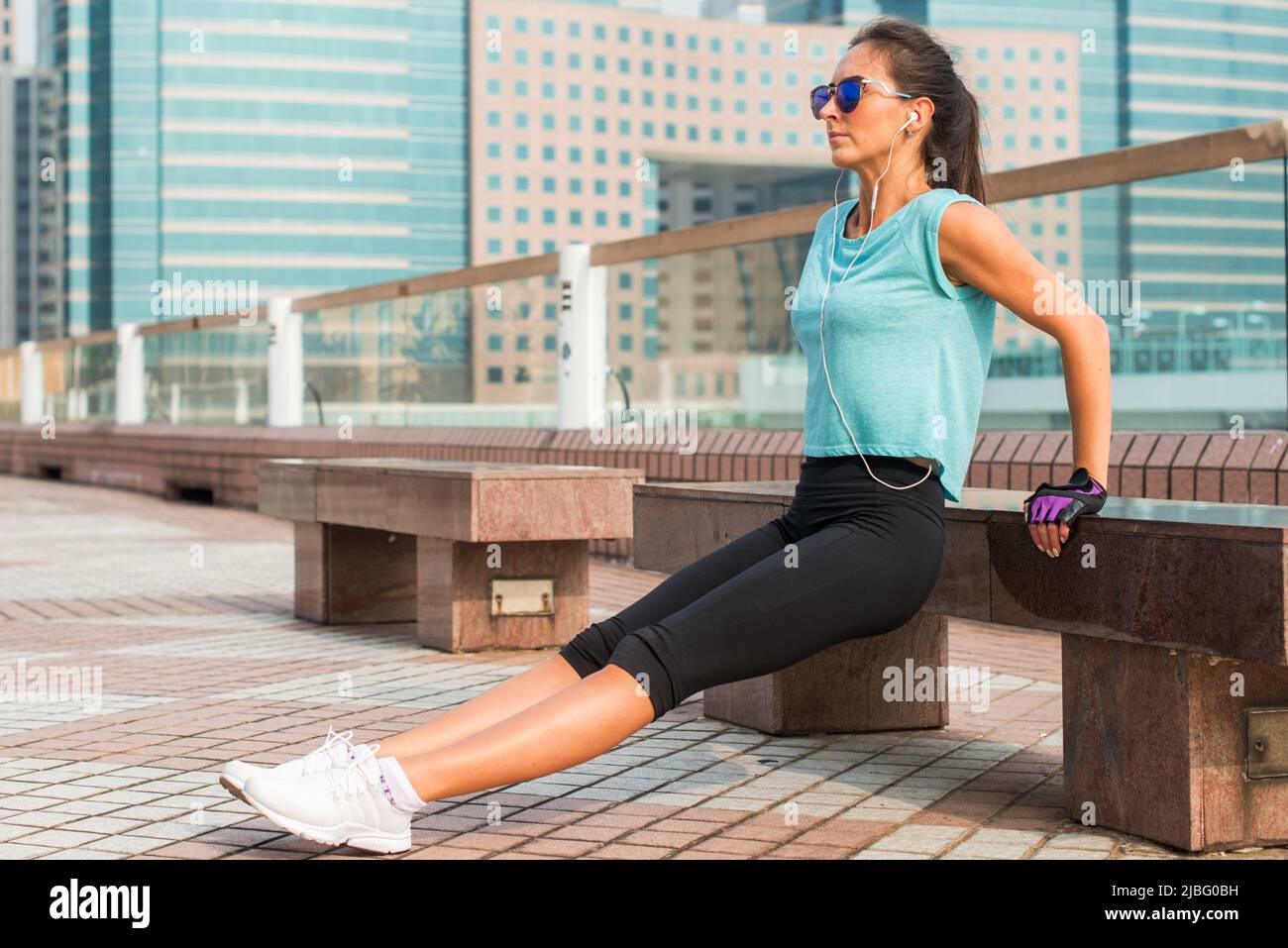 Fit donna che fa tricipiti panca tuffa l'esercitazione mentre ascolta la musica nelle cuffie. Fitness ragazza che si allenano in città. Foto Stock