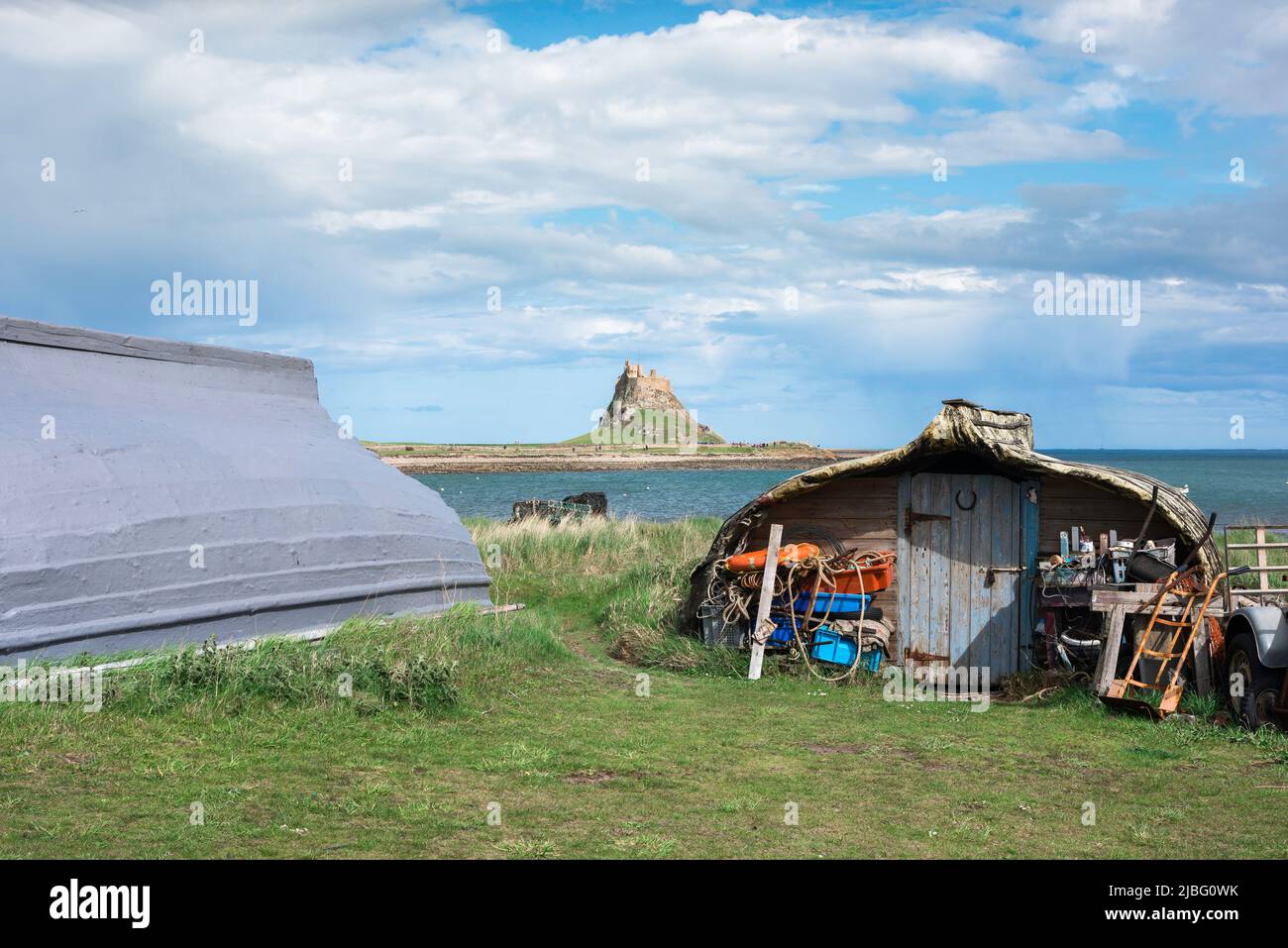 Holy Island UK, vista di battelli da pesca convertiti nella zona del porto di Holy Island con il castello di Lindisfarne in lontananza, Northumberland, Regno Unito Foto Stock
