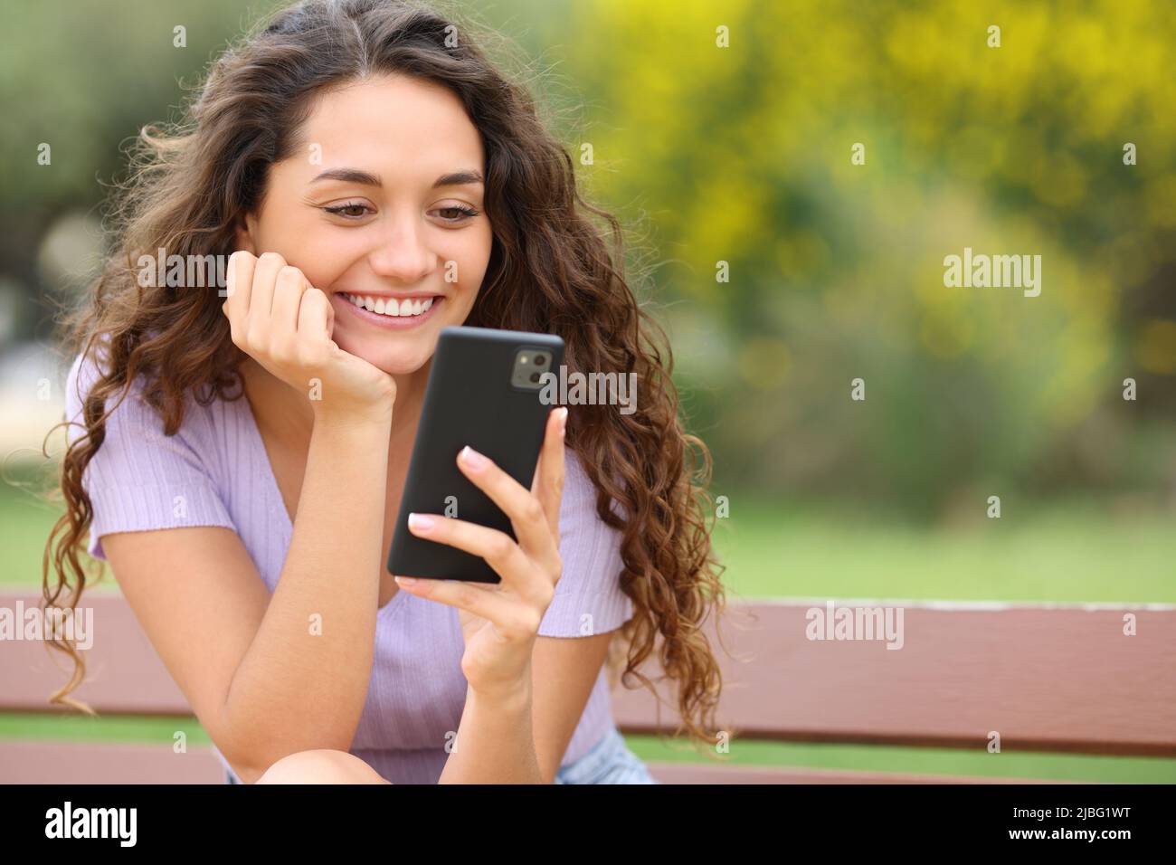 Donna felice con smartphone e sorridente seduto in un parco Foto Stock