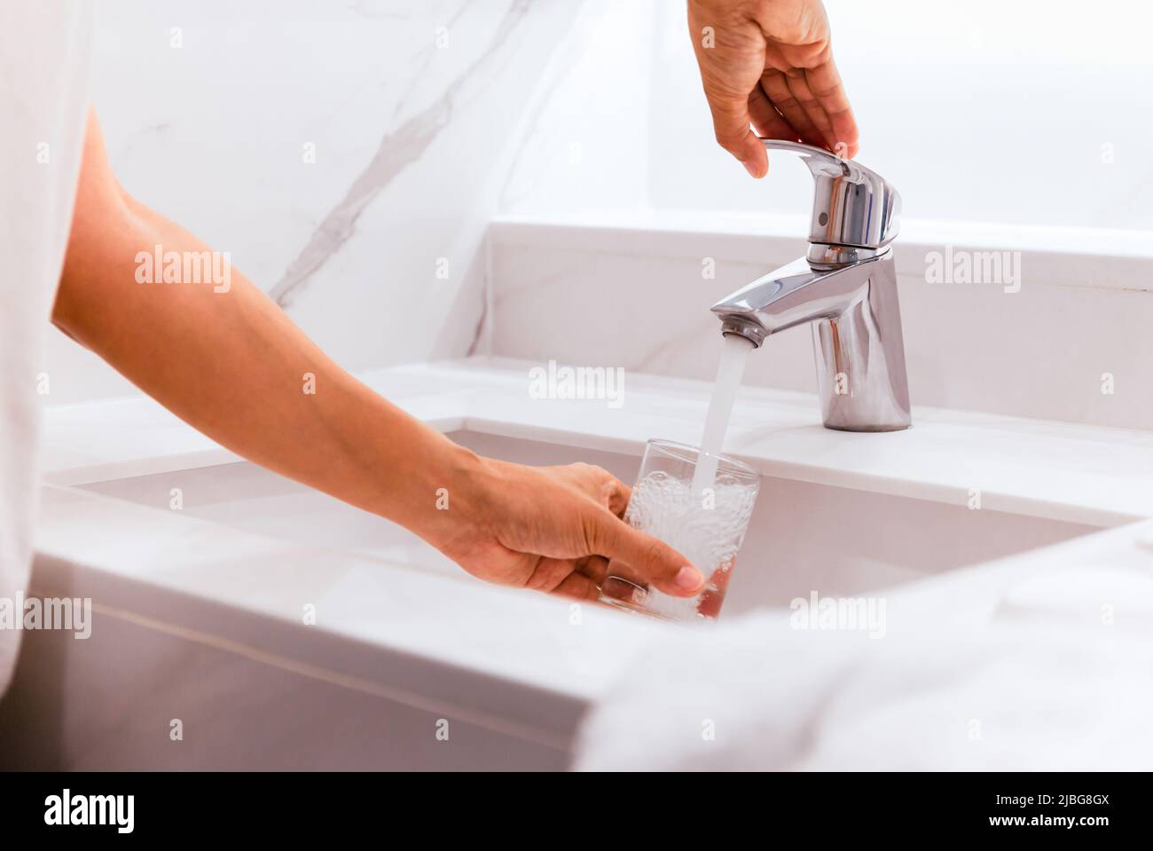 Uomo che riempie il bicchiere d'acqua al lavandino in bagno. Foto Stock