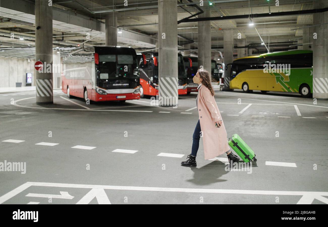 Donna viaggiatore con FFP2 respiratore che passa attraverso la stazione degli autobus con i bagagli. Viaggiare durante pandemia covida. Foto Stock