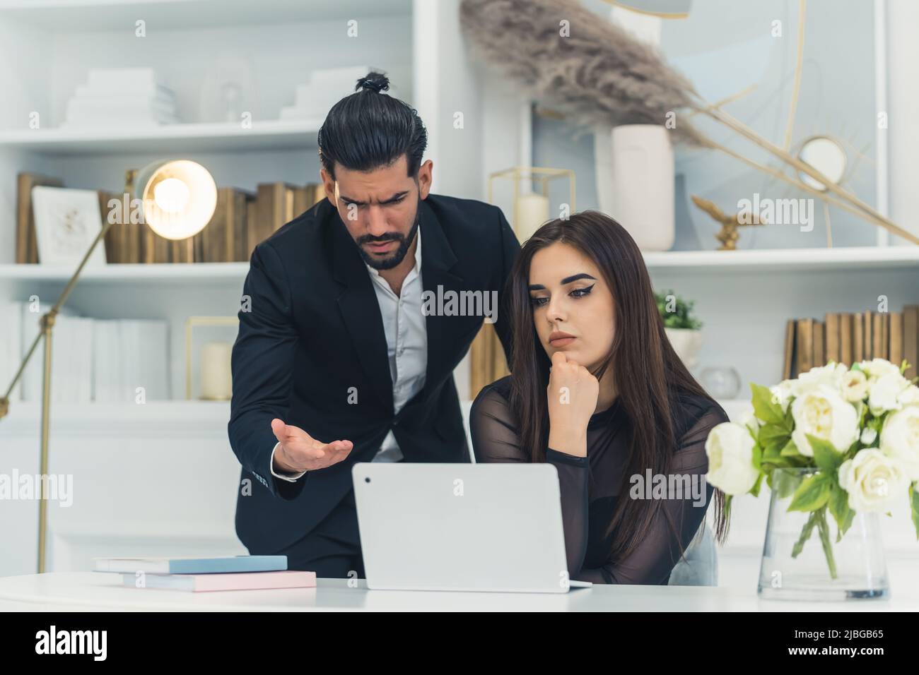 Brunette piuttosto elegante donna d'affari caucasica seduta su una sedia di fronte a un computer portatile. Infelice bearded l'uomo cubano che poiting allo schermo che osserva insoddisfatto. Foto di alta qualità Foto Stock