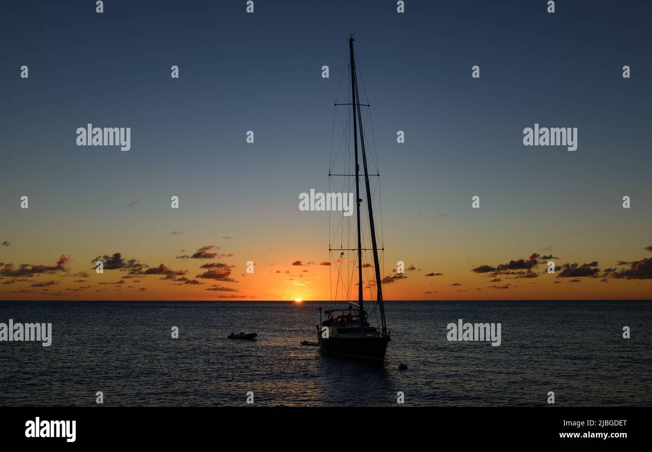 Sonnenuntergang bei Mustique - Saint Vincent e Grenadine mit Segelyacht im Hintergrund Foto Stock