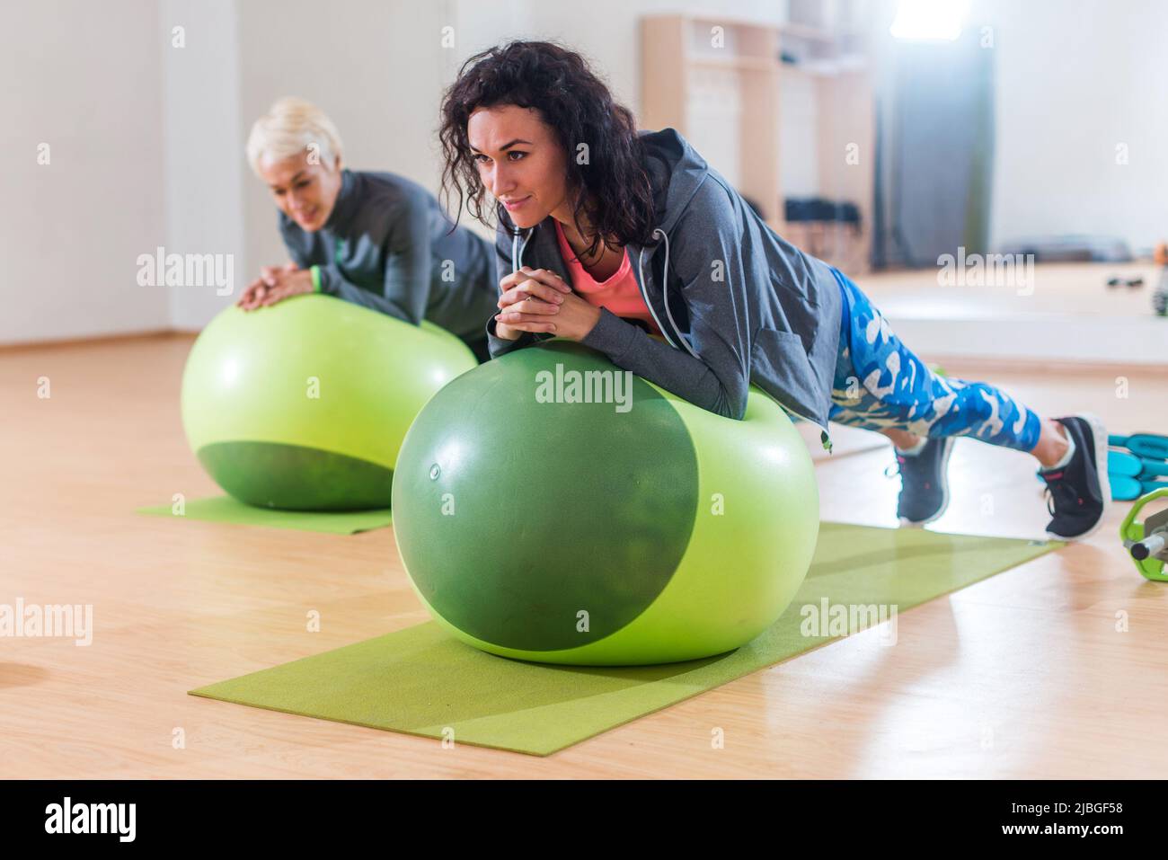 Due donne positive che fanno l'esercitazione della tavola che giace sulla sfera di equilibrio in palestra. Foto Stock