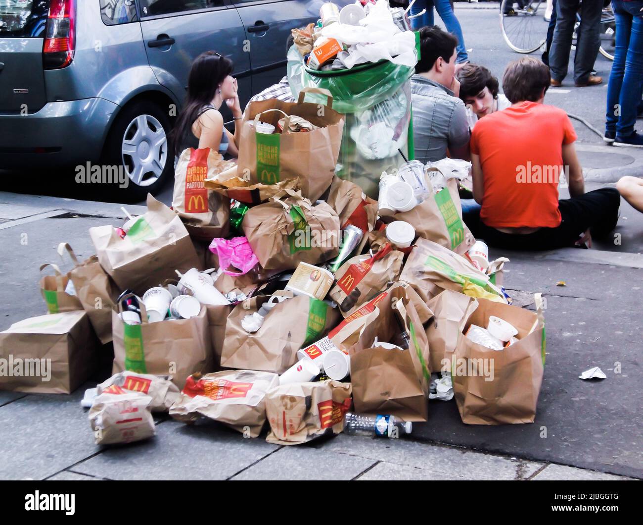 Parigi, Francia - 11 giugno 2011 : giovani seduti in strada vicino al McDonald's. La spazzatura può traboccare di rifiuti, sacchetti di carta e resti di pasti Foto Stock
