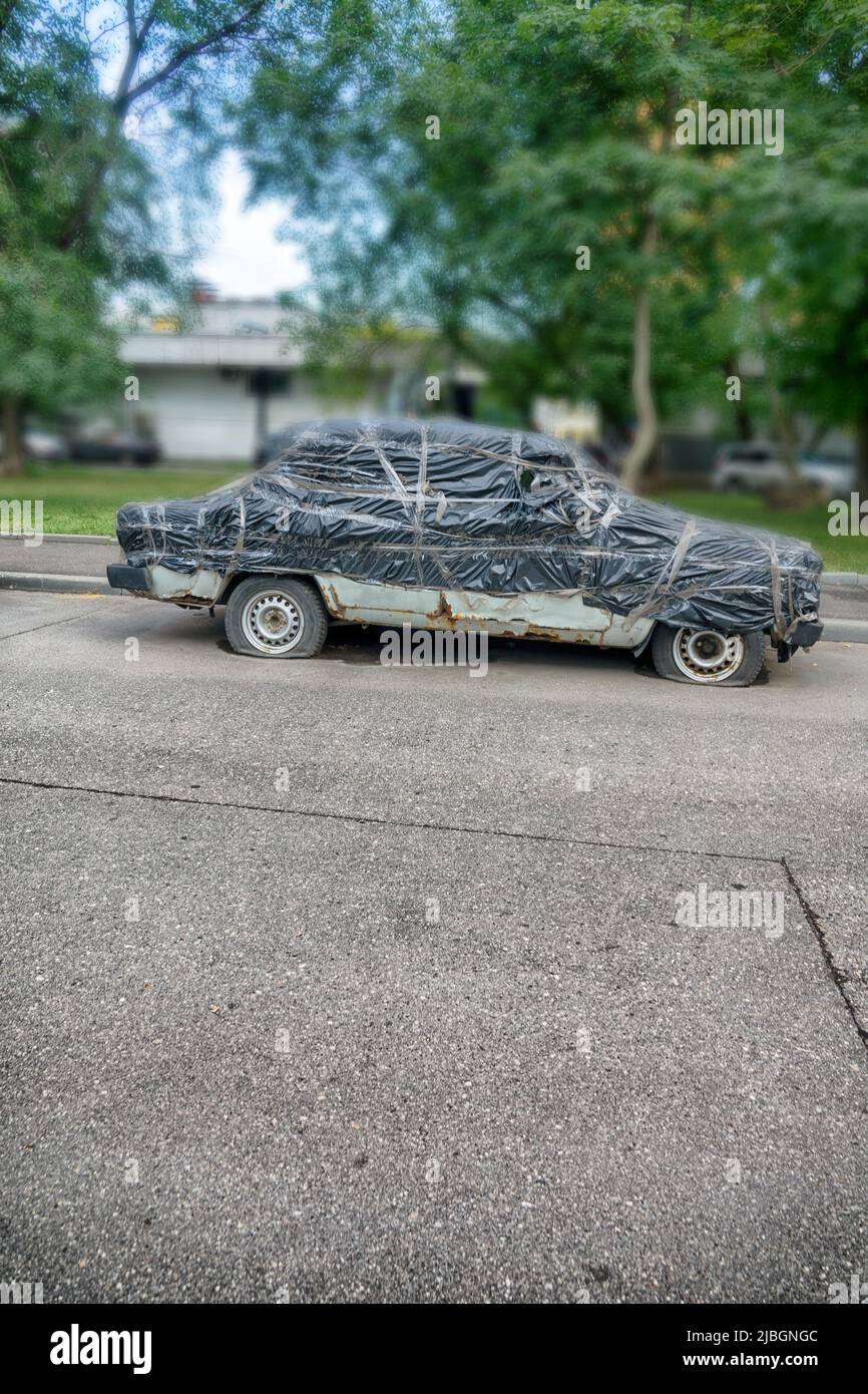 Vecchia macchina russa Lada sotto una copertura per auto. Una curiosità, una stranezza divertente. Isolato su sfondo bianco Foto Stock