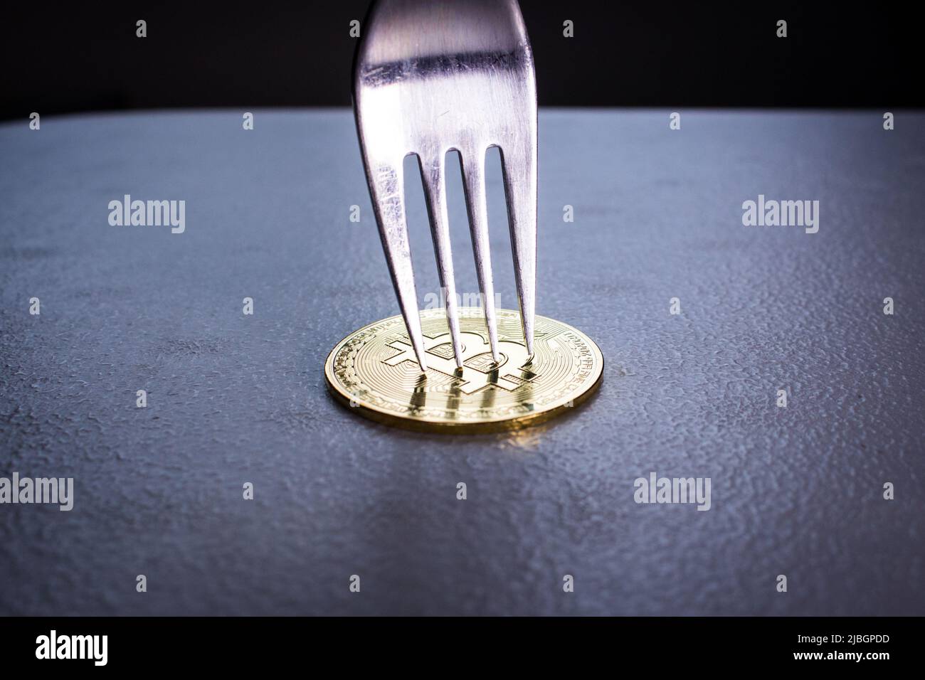 Immagine concettuale di Bitcoin Hard Fork (catena a blocchi). Forcella d'argento con Bitcoin dorato. La moneta di criptovaluta sotto la forcella è sul tavolo al buio. Foto Stock