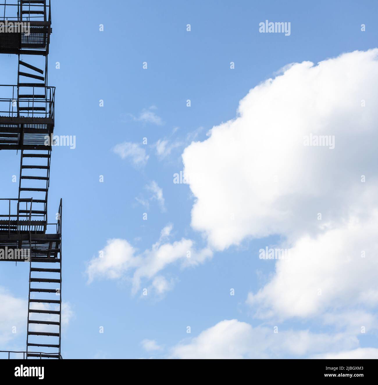 Silhouette di una fuga di fuoco su un alto edificio contro un cielo blu con le nuvole. Alcune delle scale sono rotte. Spazio libero per il testo Foto Stock