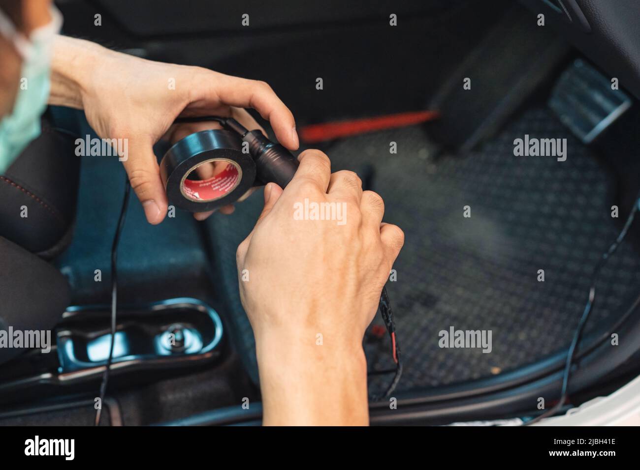 Mano del meccanico che utilizza il filo di avvolgimento del nastro per condotti dell'auto per installare il dispositivo elettronico Foto Stock