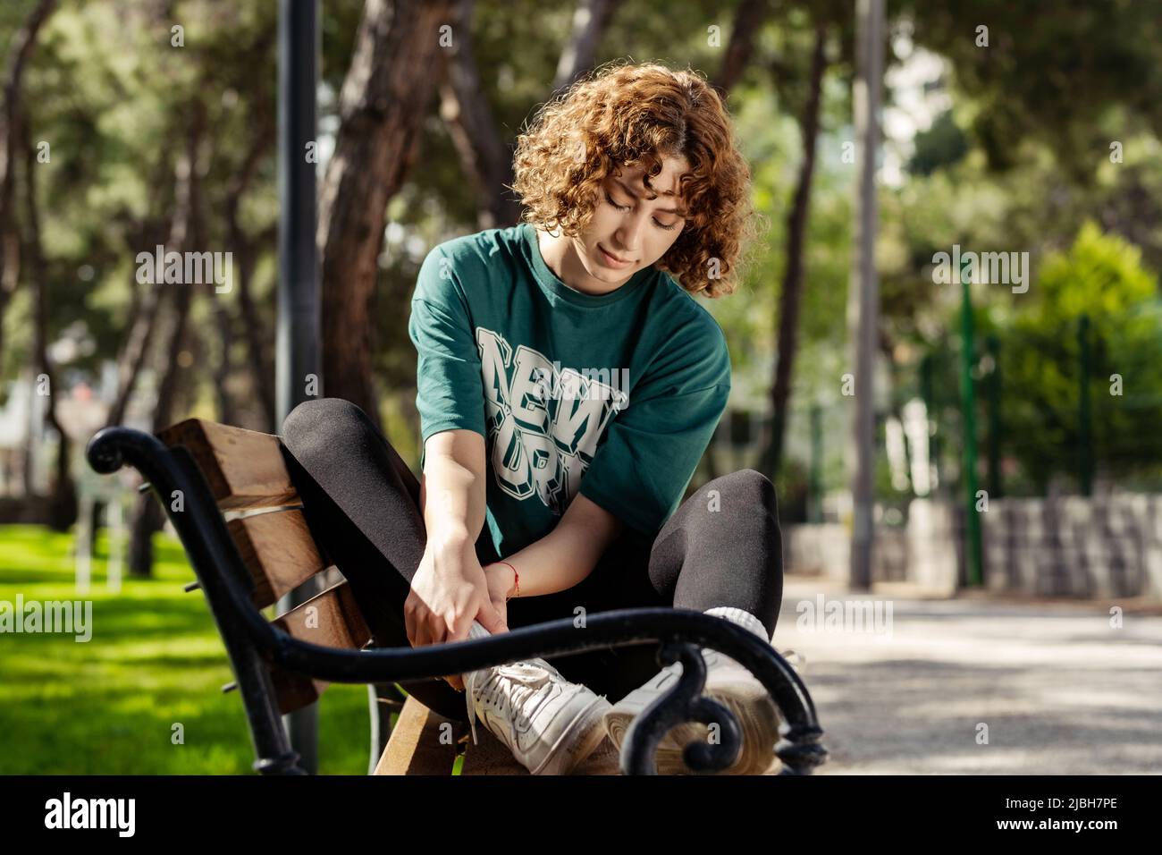 Bella donna rossa che indossa abiti sportivi in piedi sul parco cittadino, all'aperto che soffre di una lesione alla caviglia durante l'esercizio e la corsa. Healthcar Foto Stock