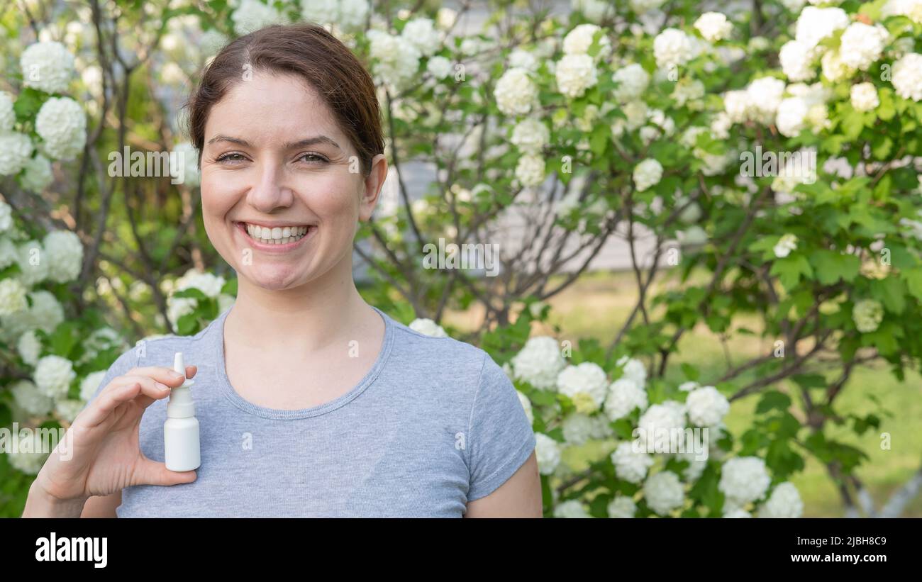 Donna felice che dimostra spray nasale sullo sfondo di un albero fiorente. Foto Stock