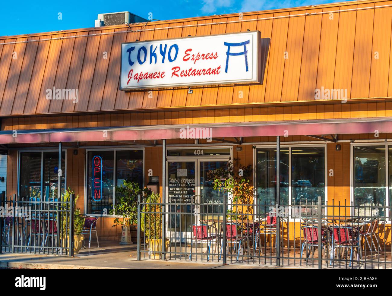 La facciata esterna del Tokyo Express Japanese Restaurant e la segnaletica con logo in rosso, bianco e blu sul tetto in metallo arancione a coste al tramonto. Foto Stock