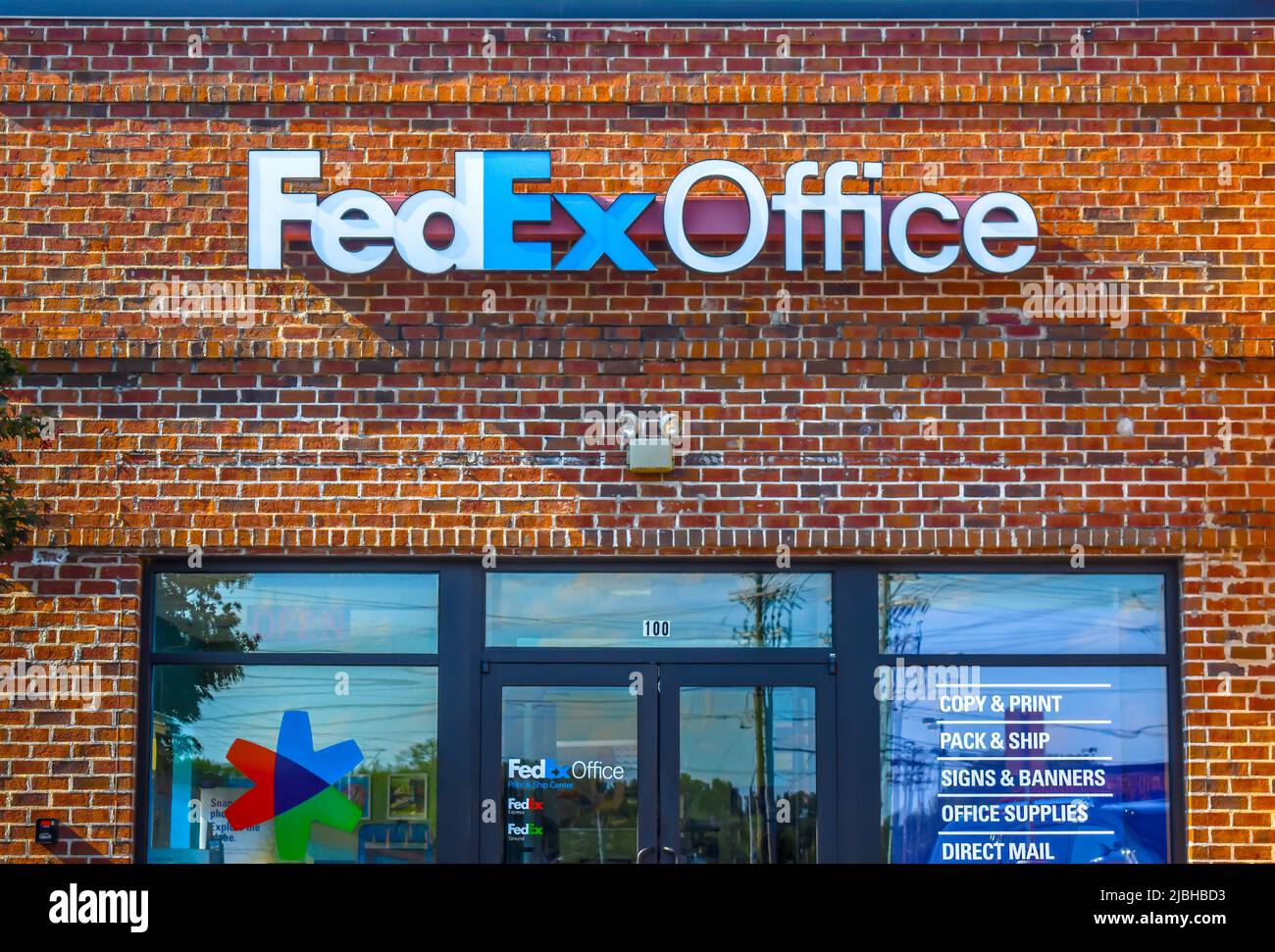 Facciata esterna FedEx Office con marchio e logo in lettere bianche e blu su un edificio in mattoni rossi sopra le finestre e le porte riflettenti. Foto Stock