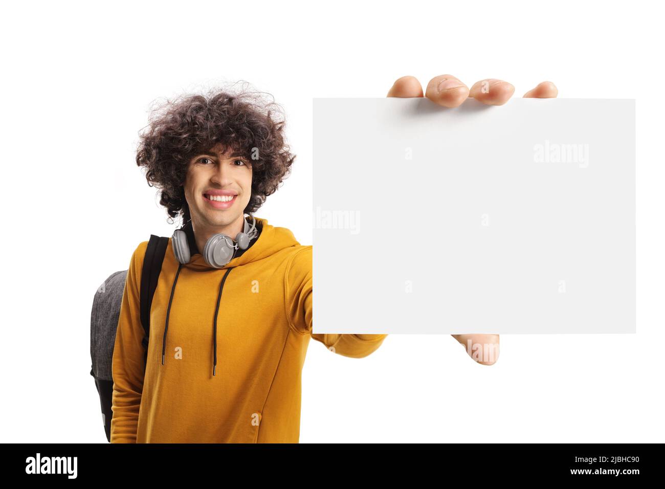 Studente maschio con uno zaino e le cuffie che mostrano una scheda vuota davanti alla fotocamera isolata su sfondo bianco Foto Stock