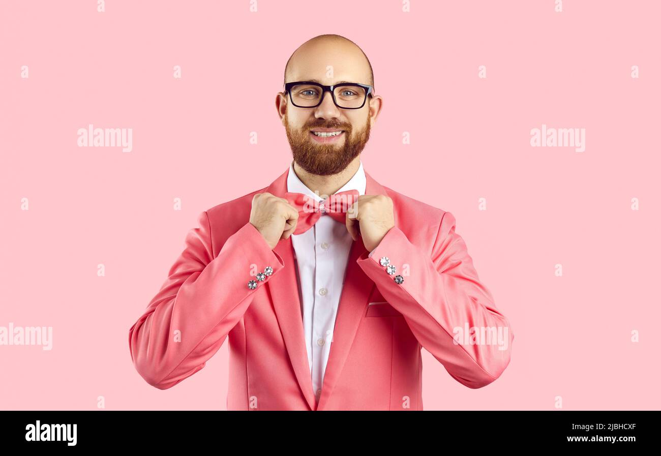 Ritratto di un uomo allegro e imponente che regola la cravatta di prua isolato su sfondo rosa. Foto Stock