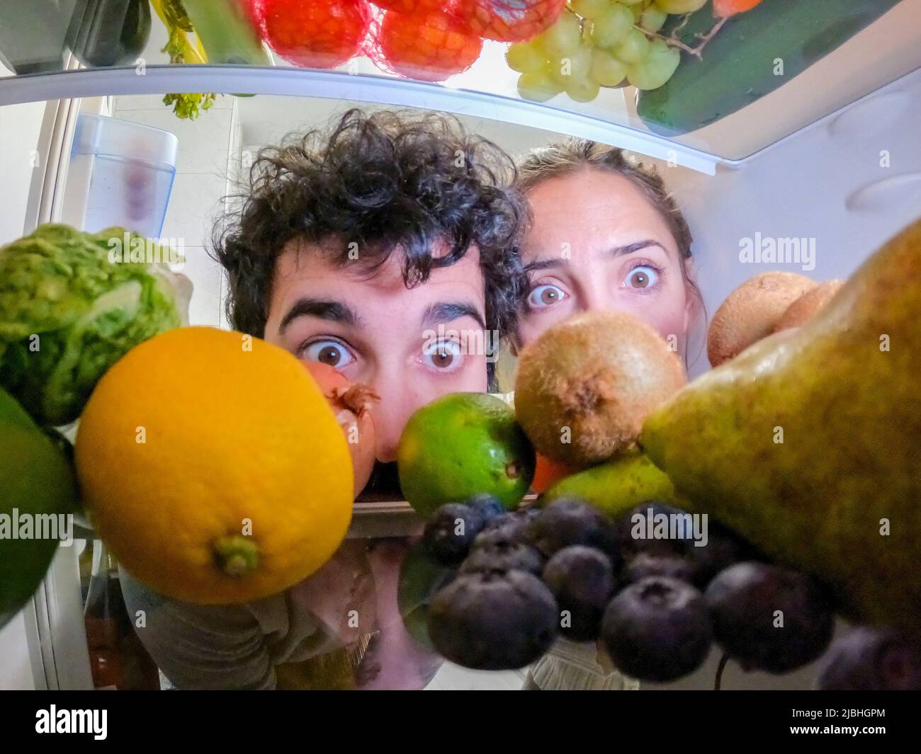 Il giovane uomo e la donna si affacciano sorpresi guardando frutta e verdura all'interno della frigda Foto Stock