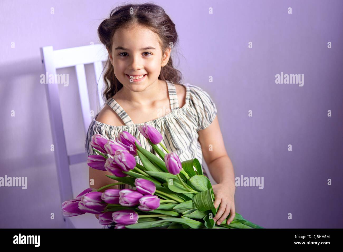 Bella bambina con un bouquet di tulipani, sullo sfondo di un muro viola Foto Stock