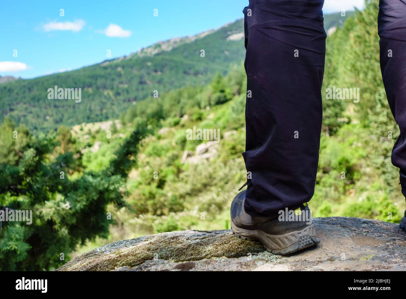 piede di un uomo che sale su una roccia e che vede il paesaggio di montagna. Foto Stock