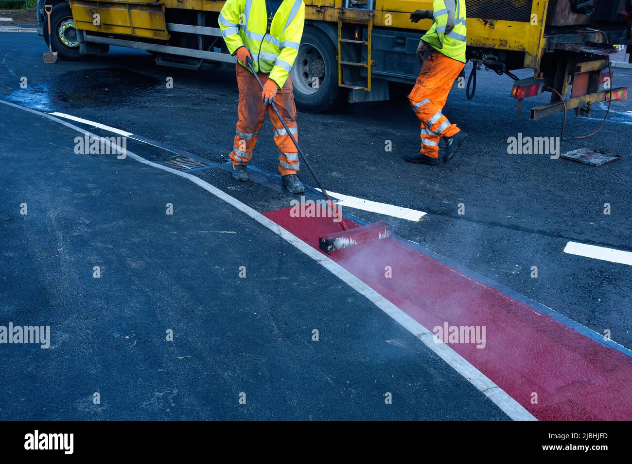 I lavoratori della strada che applicano la vernice di marcatura rossa calda sulla strada di costruzione nuova Foto Stock