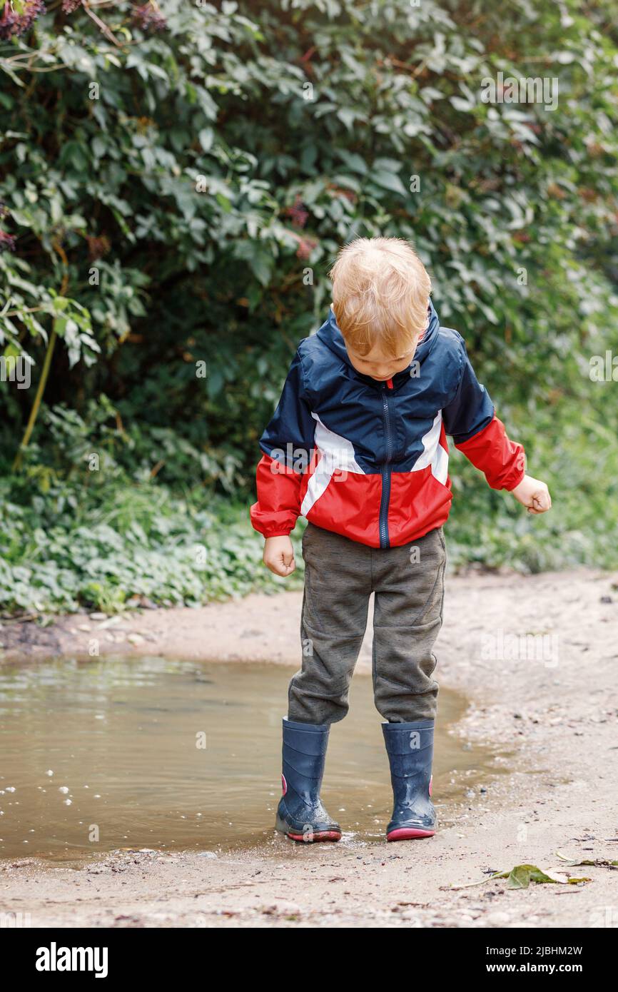 Bambino che gioca in pozzanghera. I bambini giocano all'aperto in autunno con il maltempo. Attività all'aperto in caso di pioggia in autunno per i bambini piccoli. Bambino che salta in fango pud Foto Stock