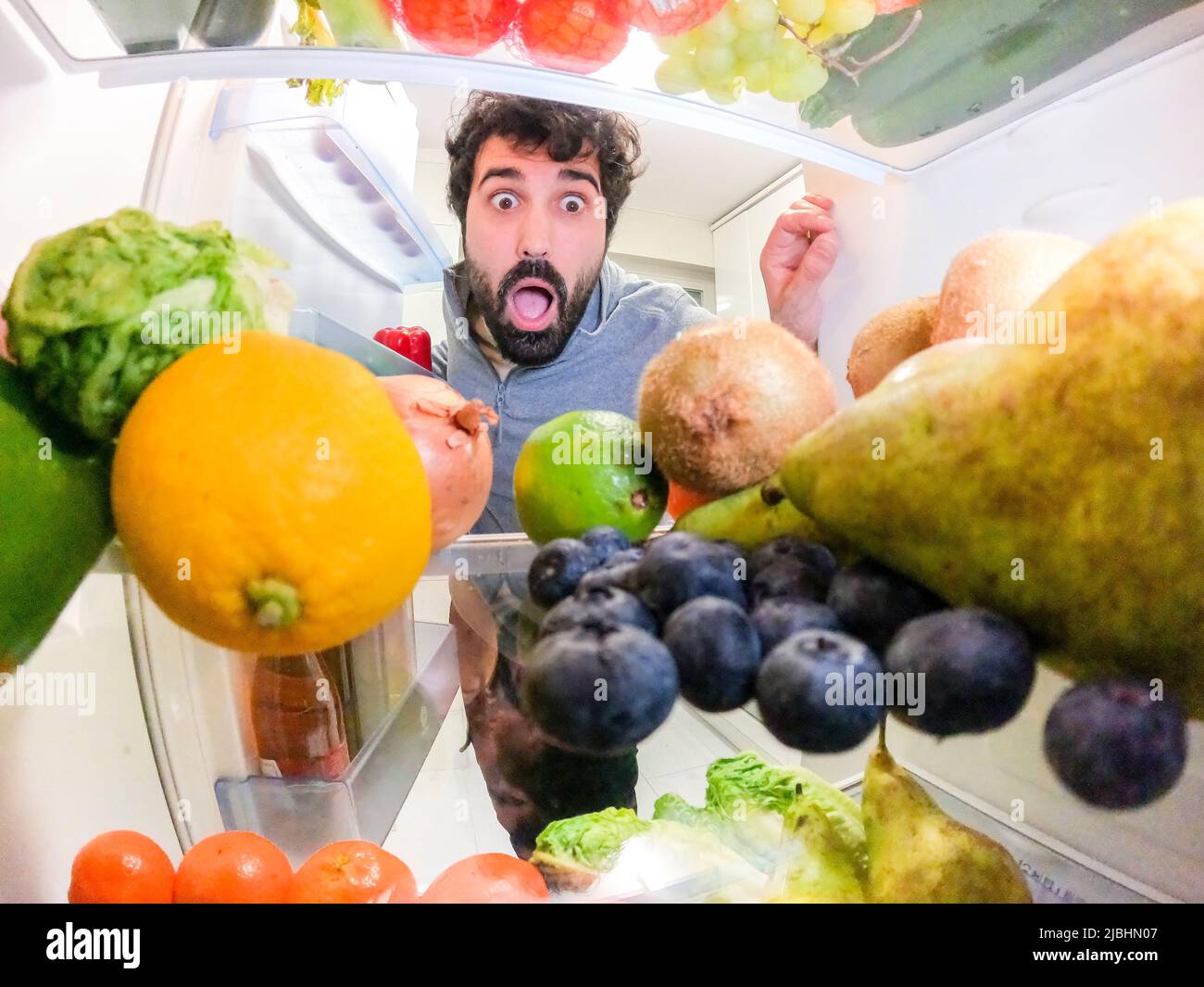 Il giovane uomo caucasico temeva di guardare la frutta e le verdure all'interno del frigorifero Foto Stock