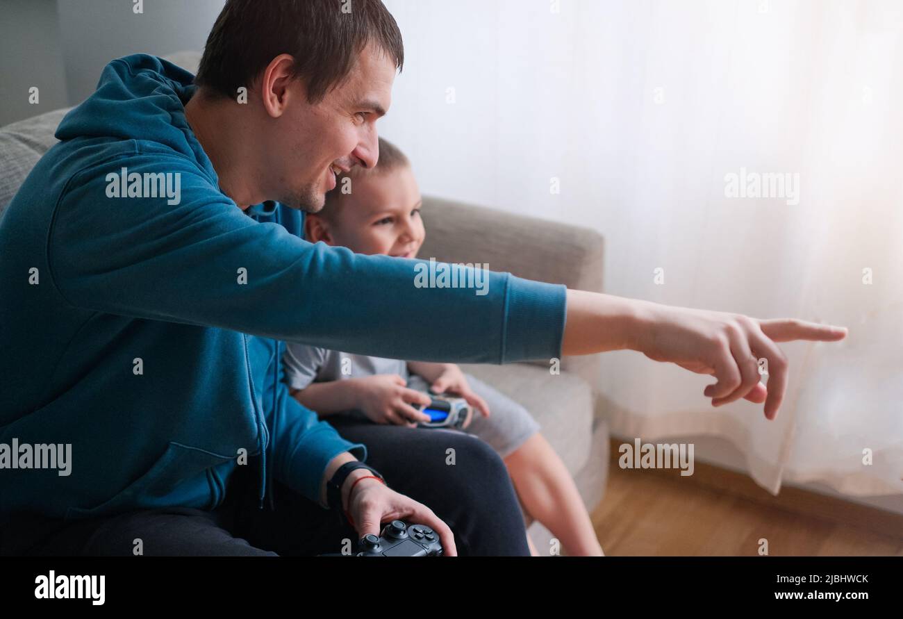 Il padre e il figlio felici si siedono nel soggiorno sul divano e giocano o guardano la TV Foto Stock