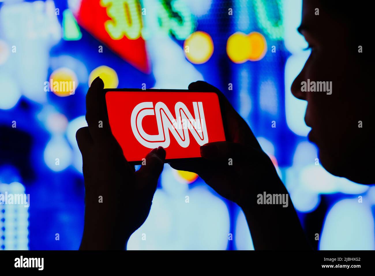 In questa foto, una donna con silhouette tiene uno smartphone con il logo della rete di notizie via cavo (CNN) visualizzato sullo schermo. Foto Stock