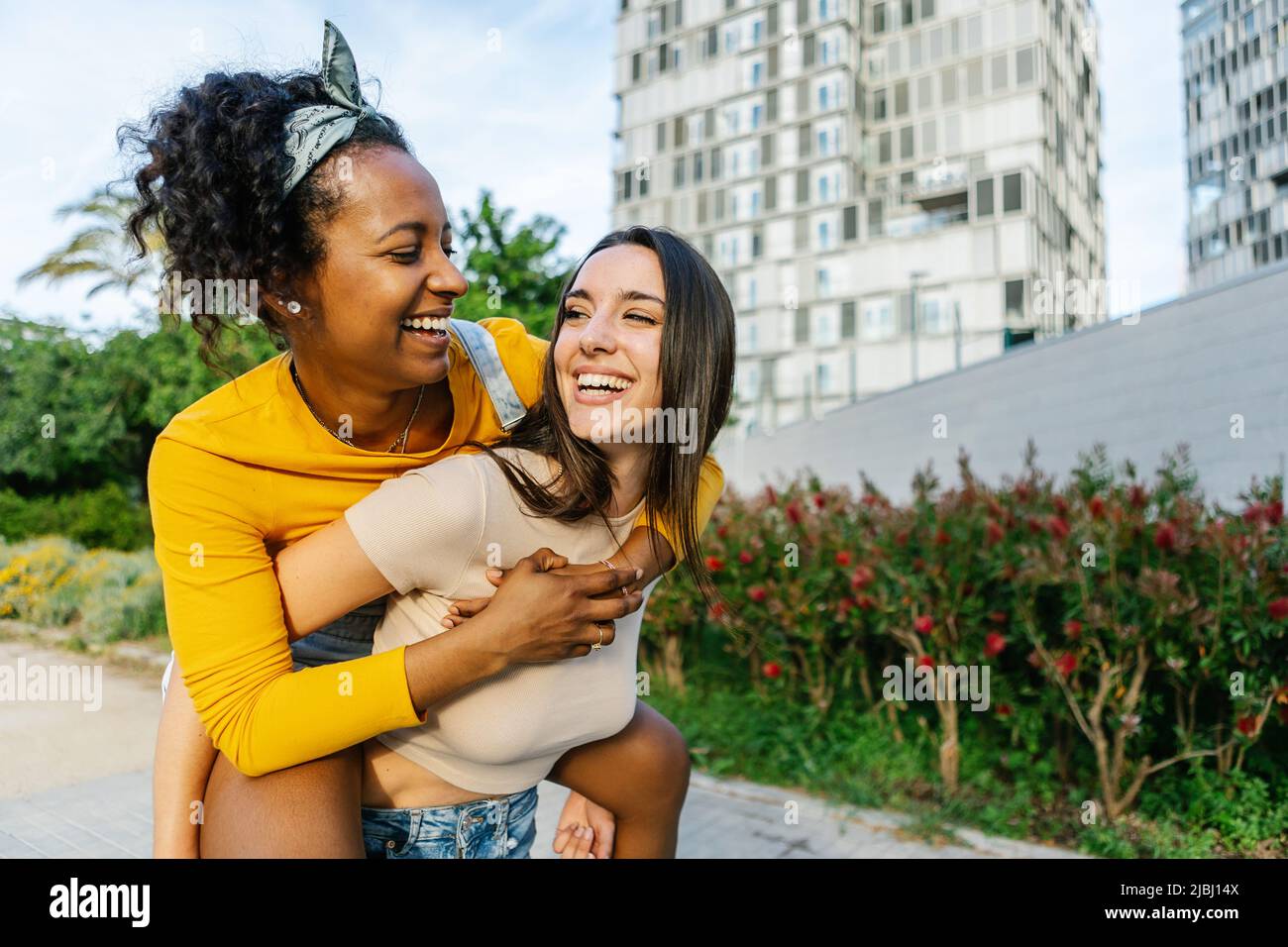 Coppia di giovani donne in amore piggybacking in strada della città Foto Stock