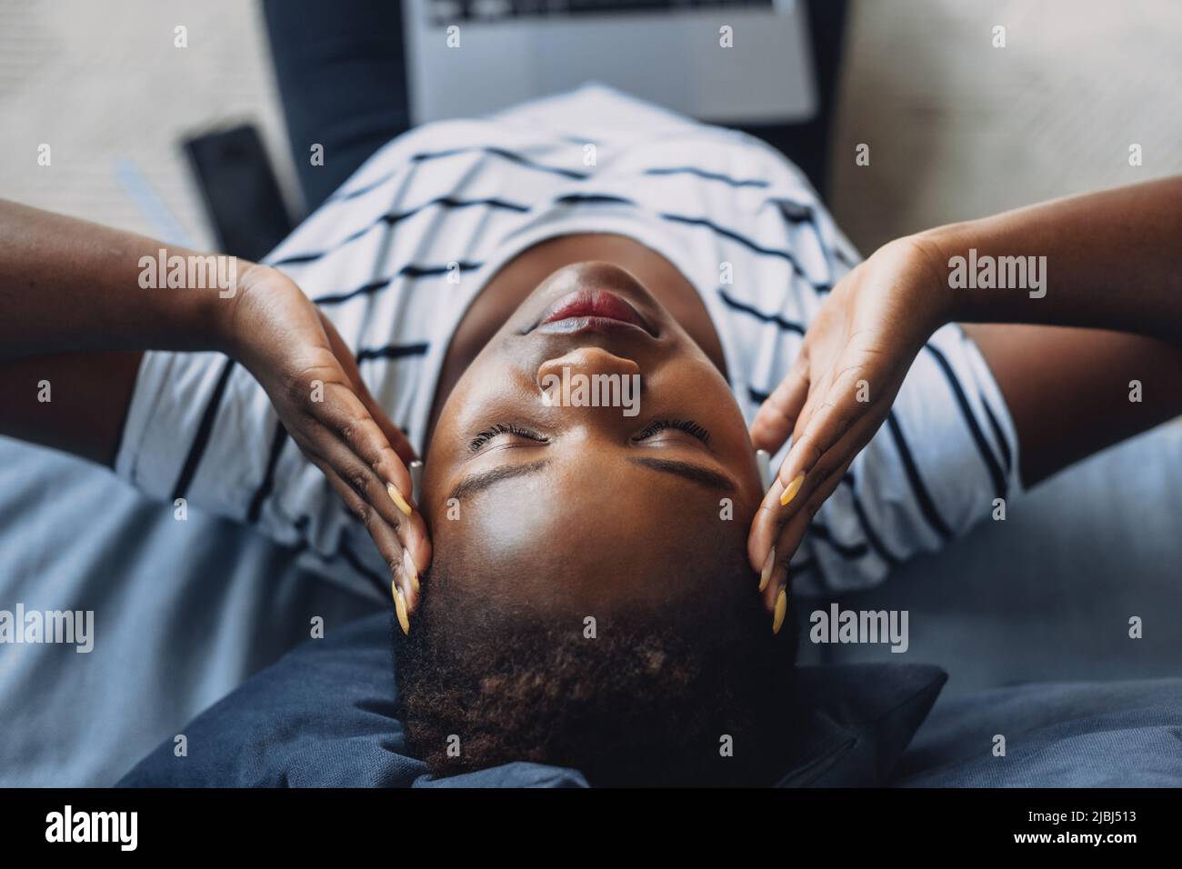 Ritratto in primo piano di una donna che afferra la testa e utilizza un computer portatile, mentre si siede a terra. Bella donna nera. Primo piano, vista dall'alto. Bellissimo africano Foto Stock