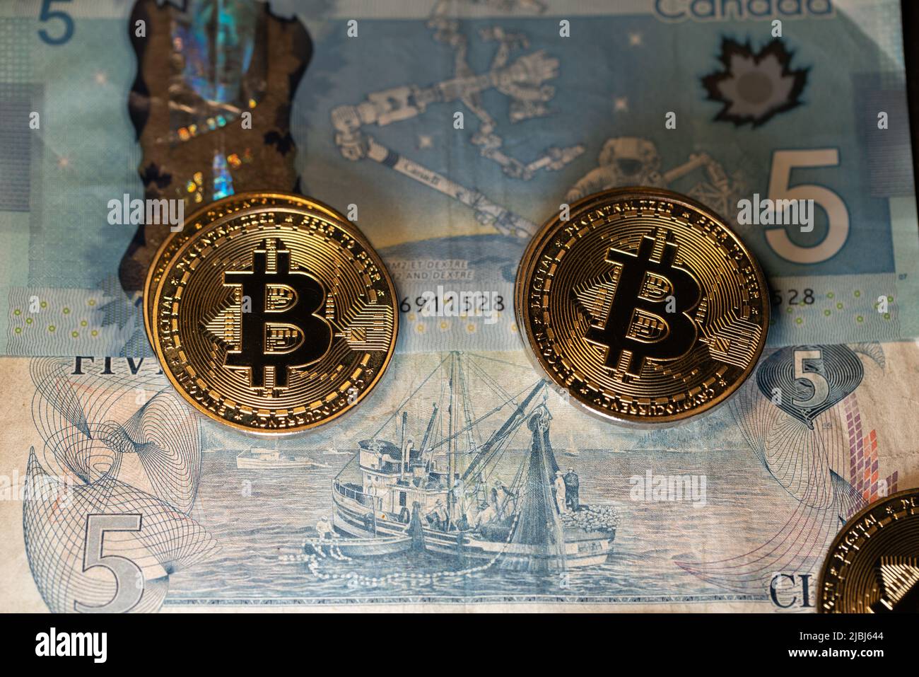 Toronto, Canada - Ottobre 30. 2021: Monete Bitcoin in cima alle banconote in dollari canadesi, scambiando BTC con CAD Foto Stock