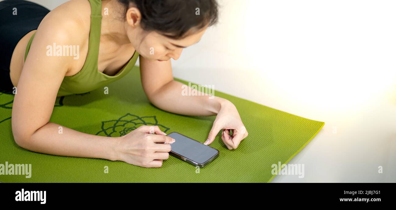 Le donne giocano in movimento e si siedono sul tappeto verde yoga mentre riposano per fare pratica in casa. Foto Stock