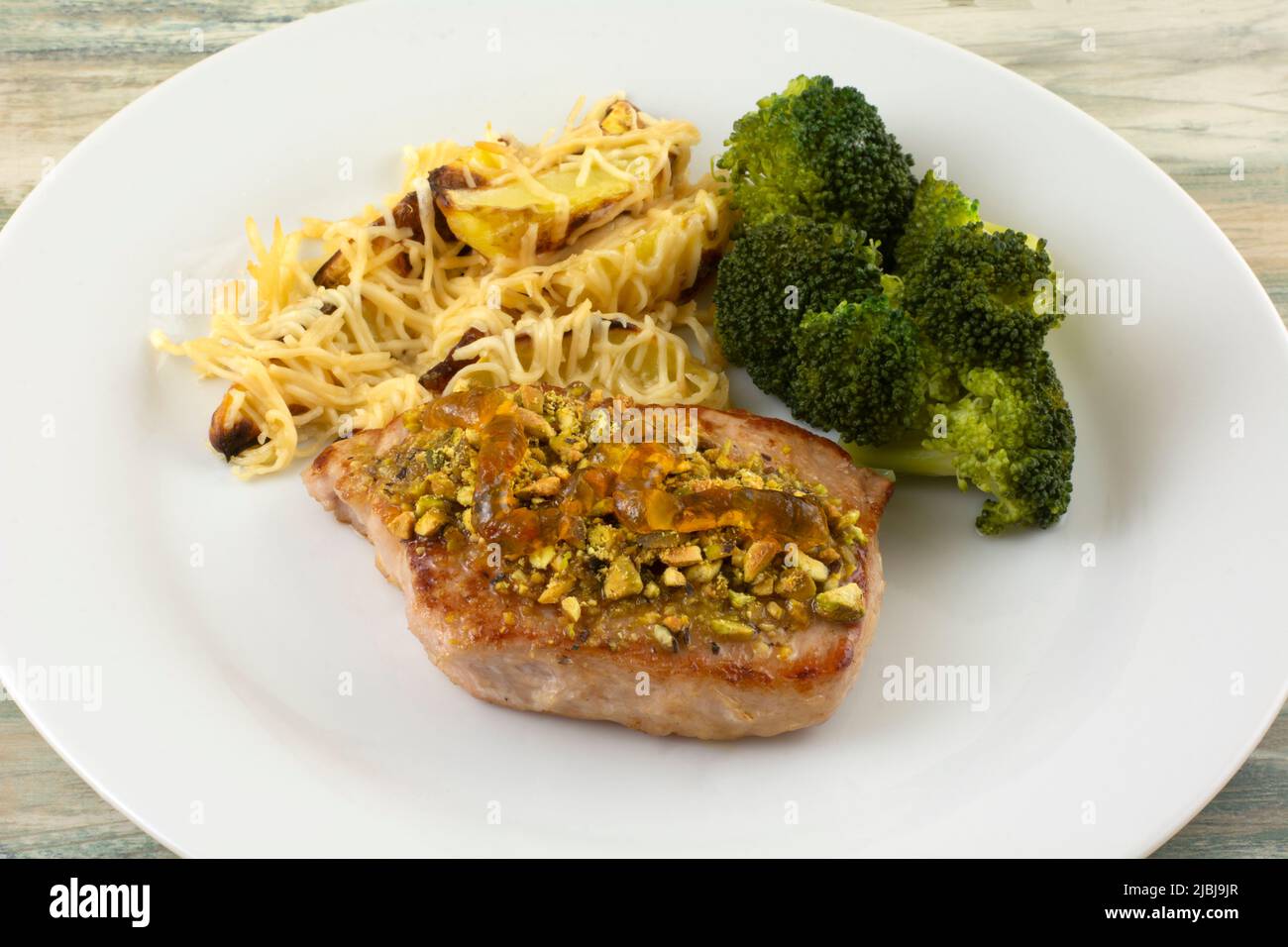 Trita di maiale con pistacchi schiacciati e marmellata d'arancia, broccoli e spicchi di patate con formaggio Foto Stock