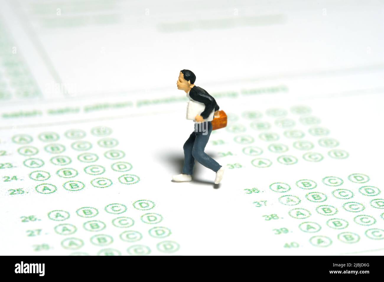 Fotografia di personaggi giocattolo in miniatura. Concetto del giorno dell'esame in ritardo. Uomini pupilla correre sopra esame rispondere foglio di carta. Foto immagine Foto Stock