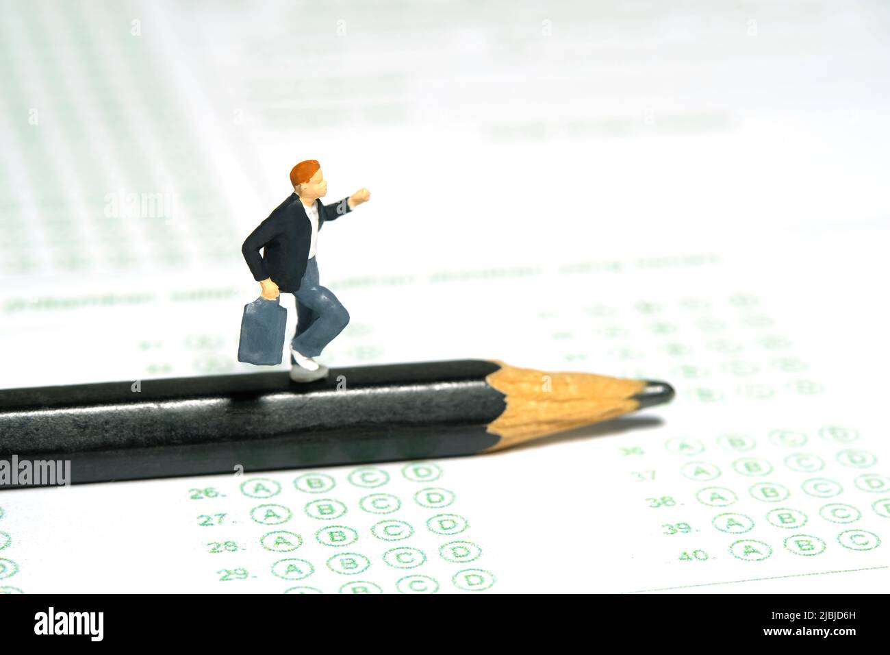 Fotografia di personaggi giocattolo in miniatura. Concetto del giorno dell'esame in ritardo. Uomini pupilla che corre sopra la matita e foglio di carta di risposta di esame. Immagine pho Foto Stock