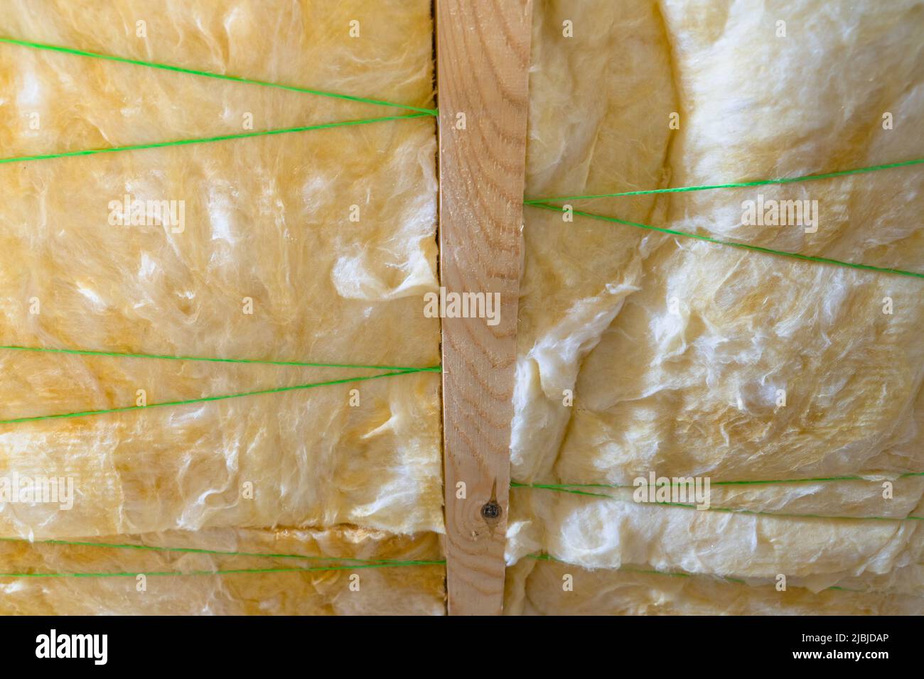 Isolamento del tetto in vetro. La filettatura in plastica dello spago supporta l'isolamento tra le travi. Primo piano di lana di vetro di colore giallo Foto Stock