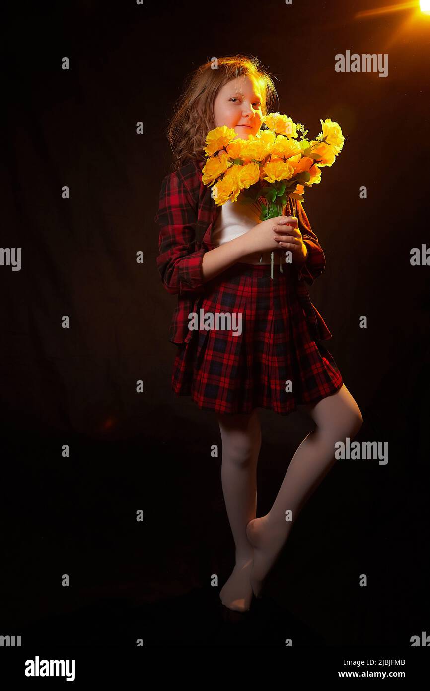 Ragazza giovane felice con fiori gialli bouquet in studio scuro con luce flash. Modello in posa su sfondo nero Foto Stock