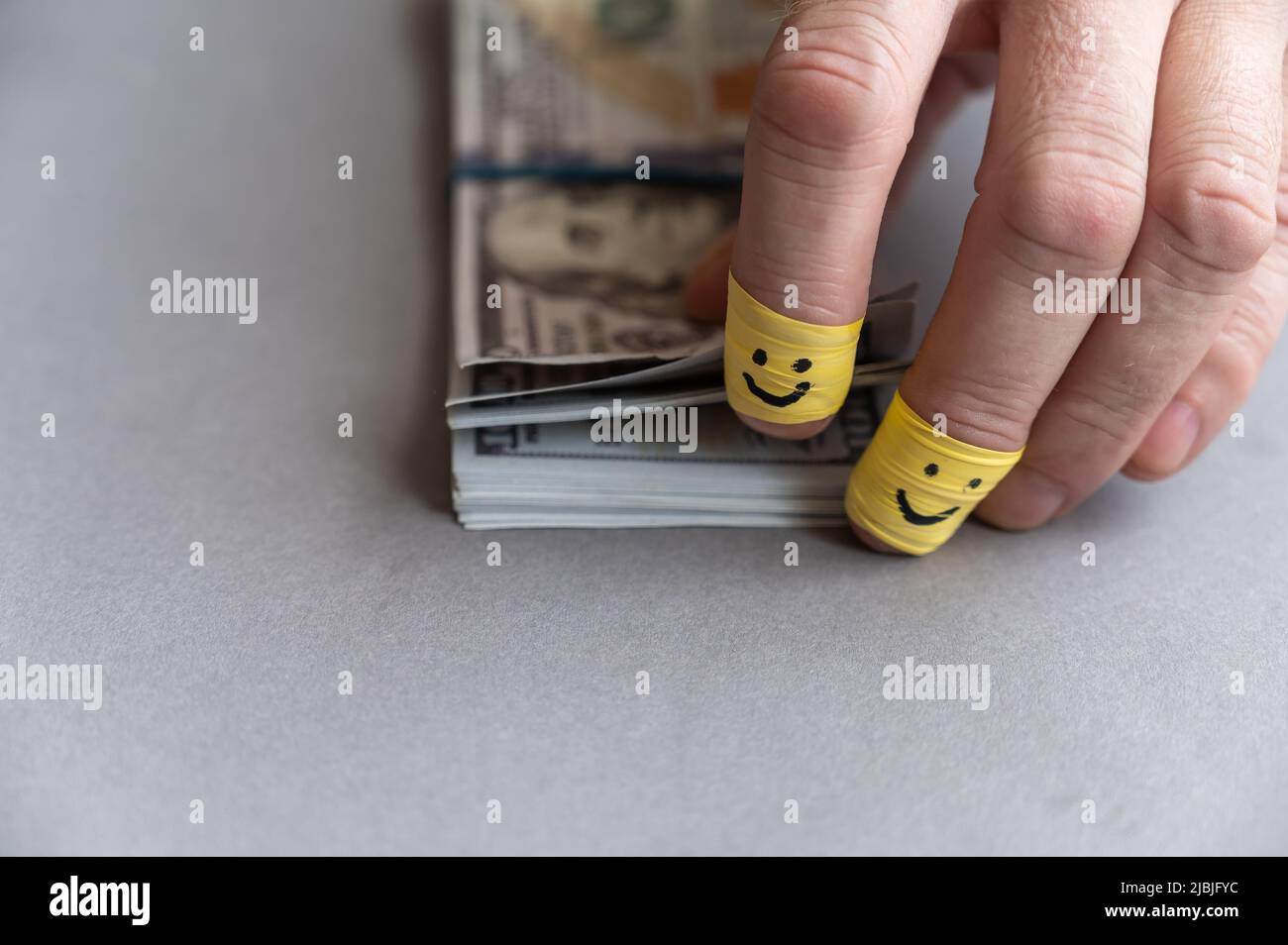 Le dita dell'uomo contano i soldi sullo sfondo grigio. WAD di dollari americani cento fatture. L'indice e le dita centrali sono avvolte in nastro giallo. Felice SM Foto Stock
