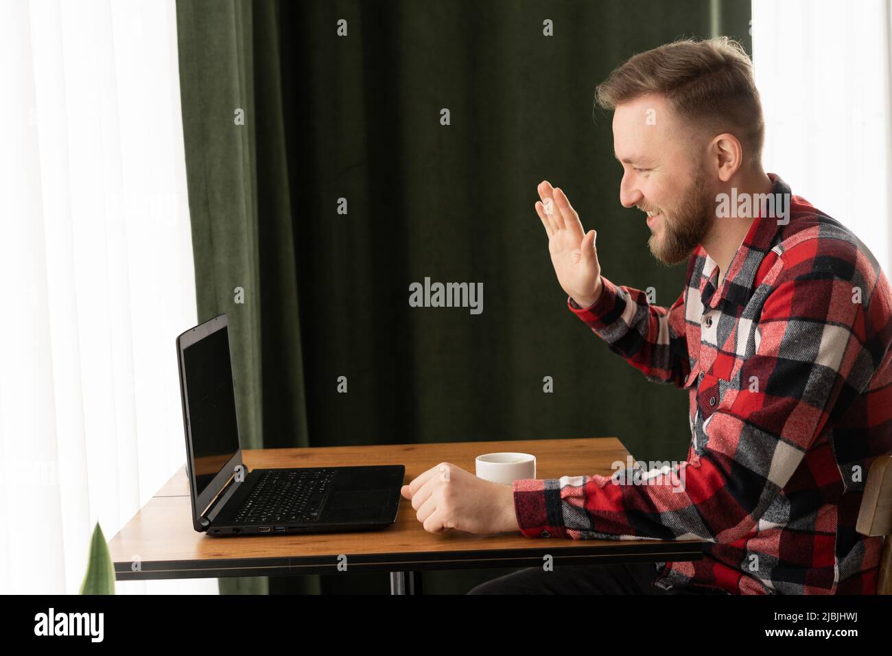 Sorridente bell'uomo che ha una videochiamata in bar, uomo d'affari bearded che parla alla videochiamata con i colleghi, freelance che prende l'ordine dal cliente via Foto Stock