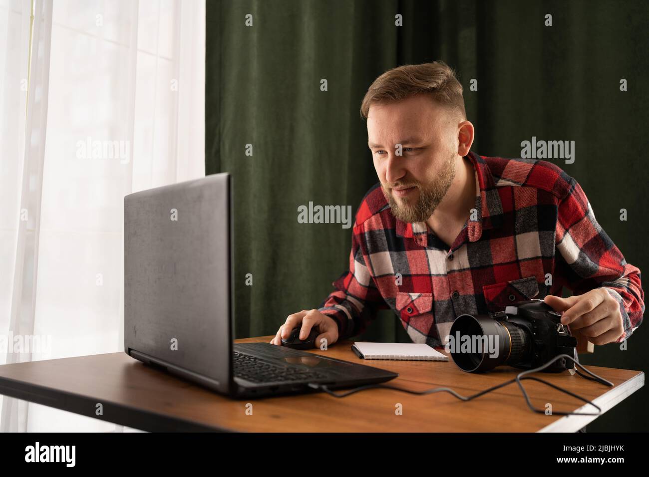 Il fotografo non carica i file sul portatile. Controllare le foto lavorando in un ufficio moderno. Modificare le sue immagini su un portatile. Foto Stock